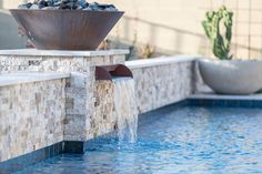 a water fountain in the middle of a pool with rocks and plants on it's sides