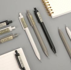 several pens, notebooks and pencils on a gray surface with writing utensils