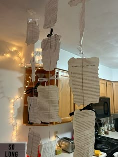 several pieces of paper hanging from the ceiling in a kitchen with string lights strung around them