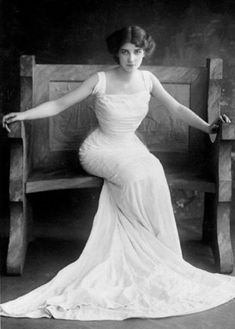 an old black and white photo of a woman in a dress sitting on a bench