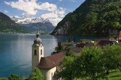 a church on the edge of a lake with mountains in the background