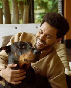 a man holding a black and brown dog on top of a couch next to a window