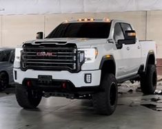 a white truck parked in a garage next to two other trucks with lights on them