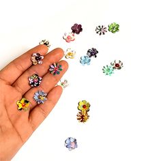 a hand holding several different colored flower shaped studs on it's thumbnail