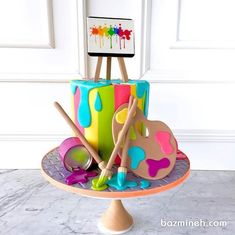 a multicolored cake with paintbrushes and an easel sitting on top