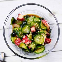 a glass bowl filled with cucumber and other vegetables next to chopsticks