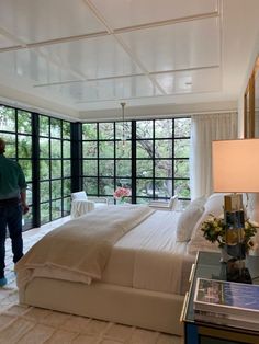 a man standing next to a large bed in a room with lots of glass windows