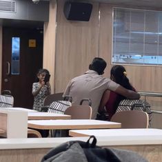 two people sitting at tables in an empty room with one person taking a photo on his phone