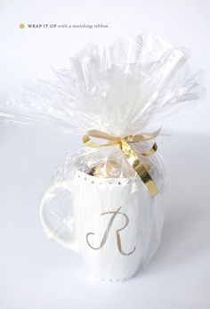 a white coffee mug filled with chocolates and wrapped in cellophane to look like a monogram