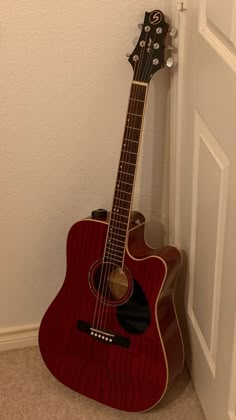 a red acoustic guitar leaning against the wall