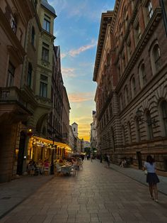 people are walking down an empty street in the middle of town at sunset or dawn