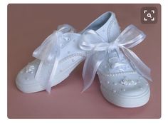 a pair of white shoes with bows and pearls on the soles are sitting on a pink surface