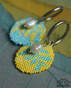 two yellow and blue beaded earrings with pearls on them sitting on a piece of fabric