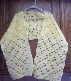 a crocheted yellow scarf hanging on a wooden hanger in front of a door