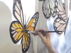 a person holding a paintbrush in front of a painting of a yellow and black butterfly