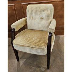 an upholstered chair with wooden legs and arm rests against a wood paneled wall