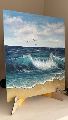 an easel with a painting of waves and birds flying over the ocean on it