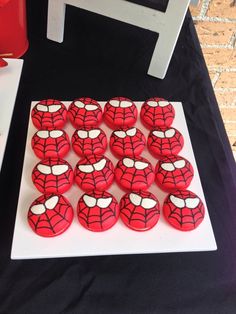 spiderman cupcakes on a white plate with black table cloth and red chair