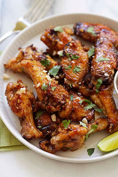 a white plate topped with chicken wings next to a side of dipping sauce and lime wedges