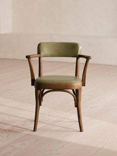 a wooden chair with green leather upholstered seat and armrests in an empty room