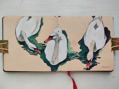 an open book with two swans painted on the front and back cover, sitting on a white surface