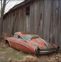 an old rusted out car sitting in front of a barn