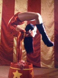 a woman is doing an acrobatic trick on top of a stool in front of a large american flag