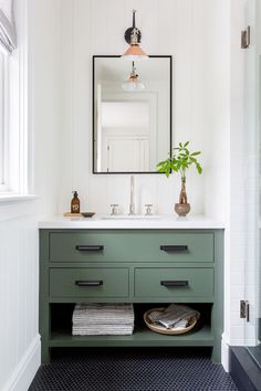 a bathroom with white walls and green drawers, black flooring and a large mirror above the sink