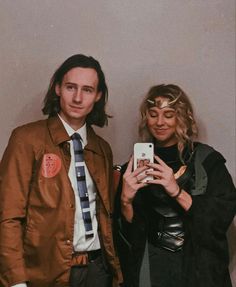 two people standing next to each other holding cell phones in front of a white wall