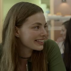 a woman with long hair smiling and wearing a green shirt in front of other women