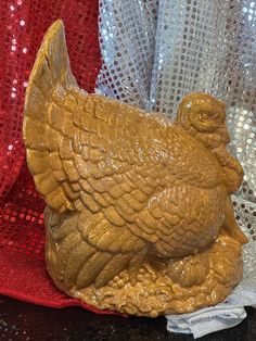 a brown chicken statue sitting on top of a table next to red and silver sequins