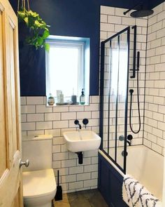 a white toilet sitting next to a bath tub in a bathroom under a window with a potted plant