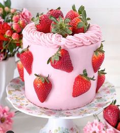 a strawberry cake with pink frosting and fresh strawberries on top, surrounded by flowers