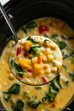 a spoon full of soup with spinach and chickpeas in it, on top of a black crock pot