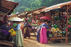 several women in colorful dresses and umbrellas at an outdoor market with flowers on display