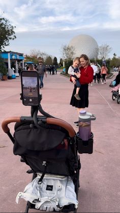 a baby in a stroller looking at something on the ground with people walking by