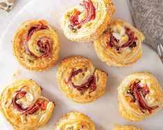 several pastries are arranged on a white platter with silverware next to them