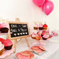 a table topped with lots of cupcakes next to a chalkboard and balloons