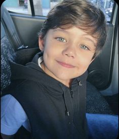 a young boy sitting in the back seat of a car with his eyes wide open