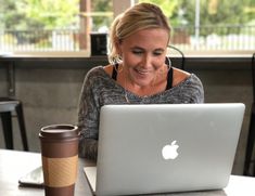 a woman sitting at a table with a laptop computer and cup of coffee in front of her