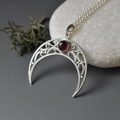 a silver necklace with a red stone sitting on top of it next to a rock