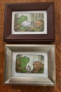 two framed pictures of frog and toad on a wooden table next to each other, one with