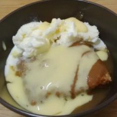 a black bowl filled with mashed potatoes and meat covered in gravy on top of a wooden table