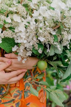 a woman holding a bouquet of white flowers and greenery with her hands on it