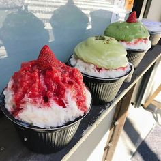 three cupcakes with different colored frosting and strawberries on top