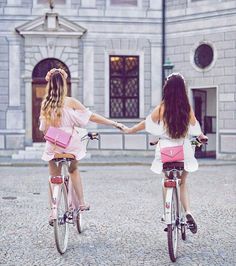 two women riding bikes holding hands in front of a large building with columns and windows