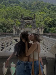 two young women kissing each other in front of a scenic area with mountains and trees