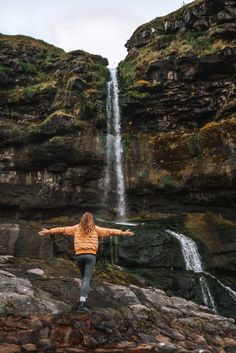 a woman standing on top of a rock next to a waterfall