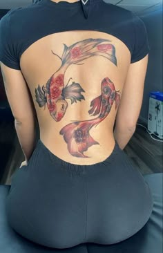 the back of a woman's body with fish and roses on her lower back