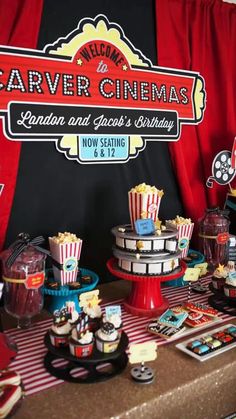 a table topped with cakes and cupcakes next to a red curtain